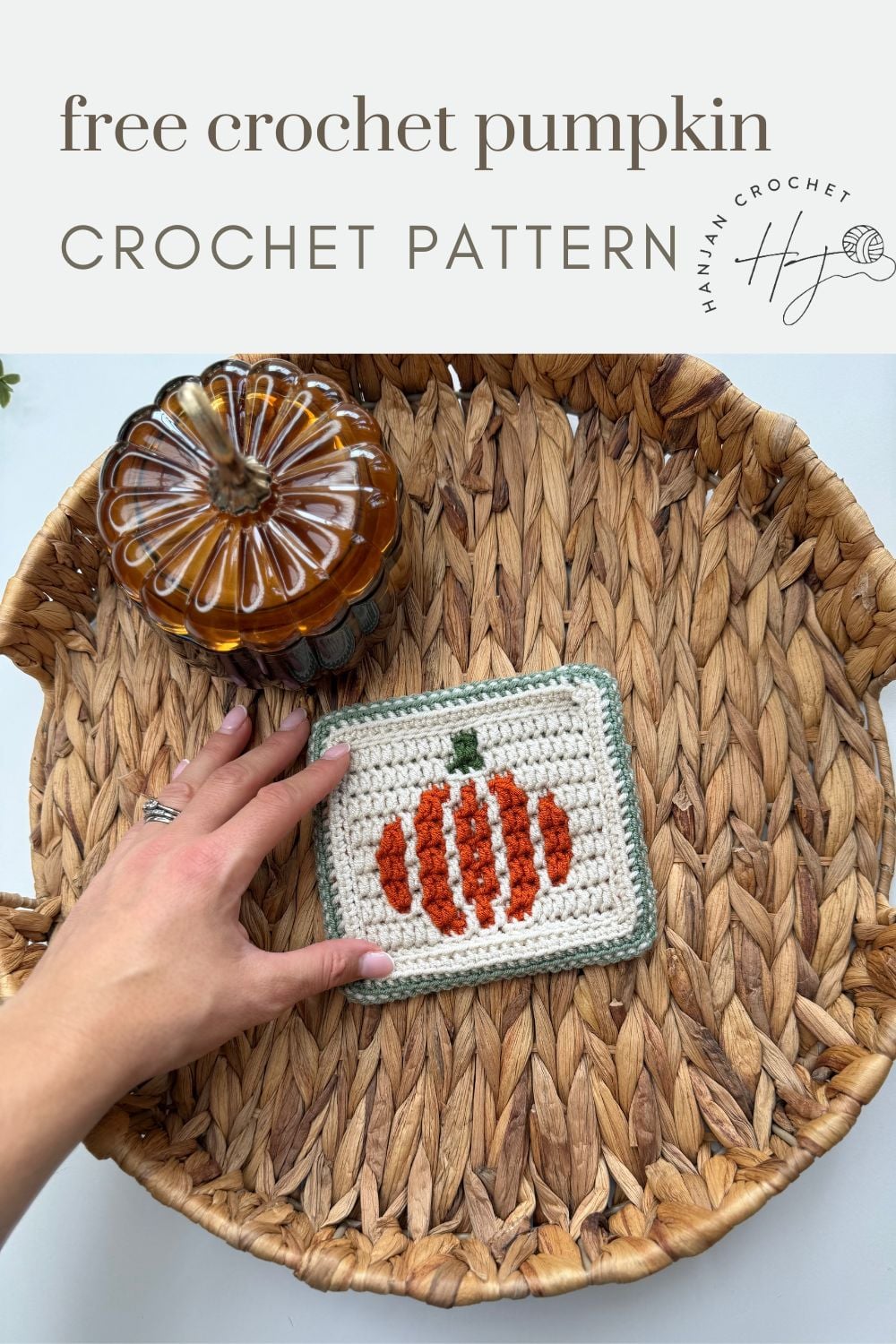 A hand holds a crocheted pumpkin coaster inside a woven basket, with a glass pumpkin ornament nearby. Text above reads “free crochet pumpkin CROCHET PATTERN.”.