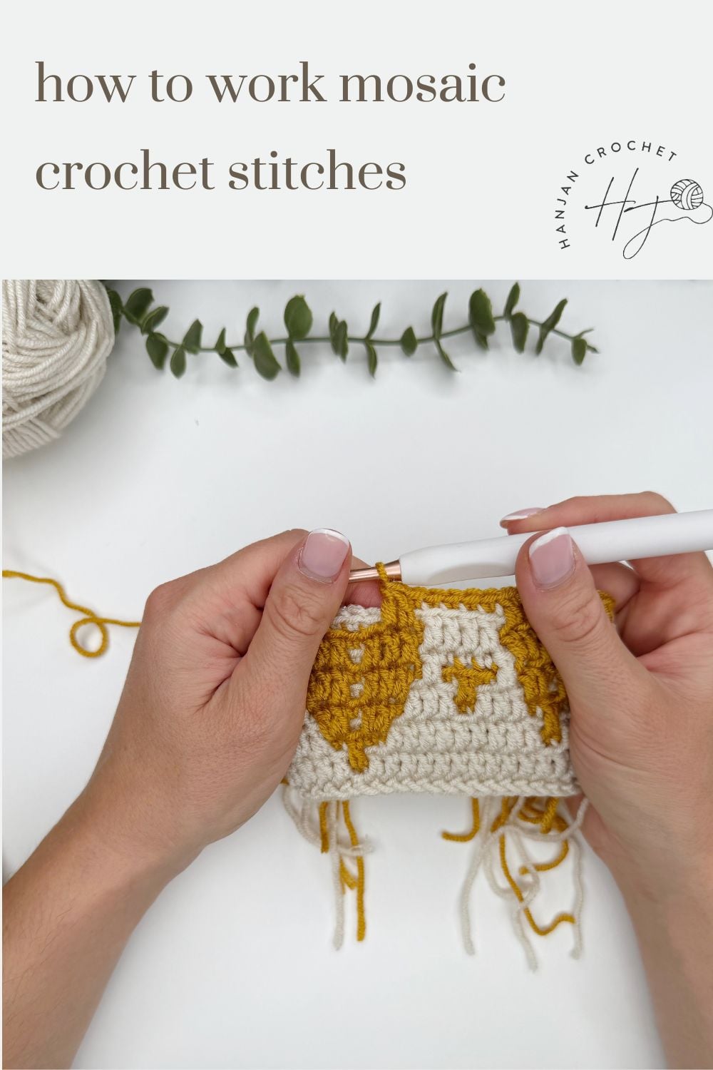 Hands holding a crochet hook and yarn, working on yellow and white mosaic crochet stitches, with yarn and greenery in the background.